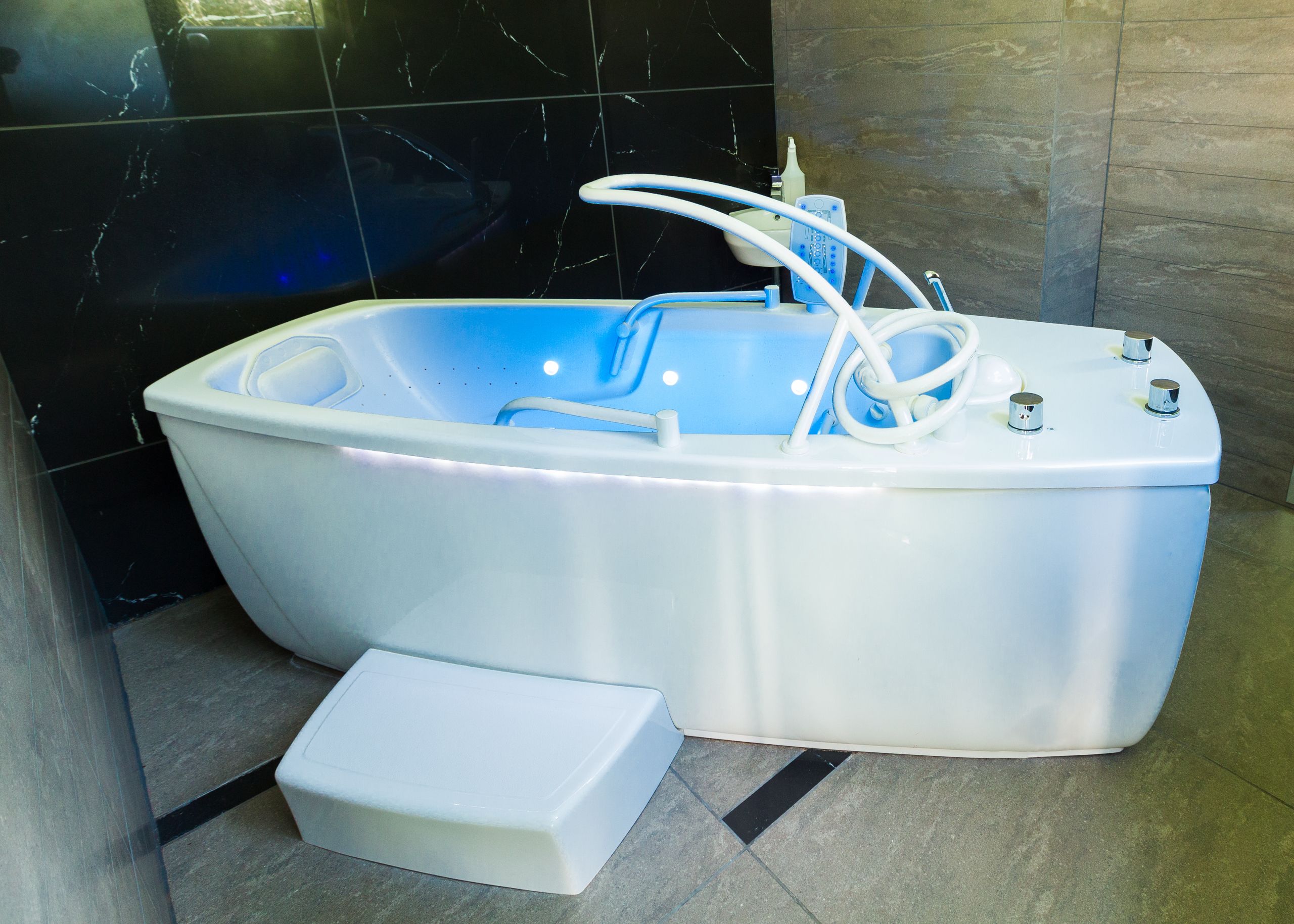 Un baño moderno con una bañera independiente, un cabezal de ducha manual y un escalón para facilitar el acceso.