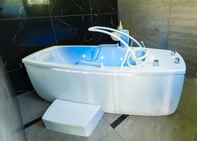 Un baño moderno con una bañera independiente, un cabezal de ducha manual y un escalón para facilitar el acceso.