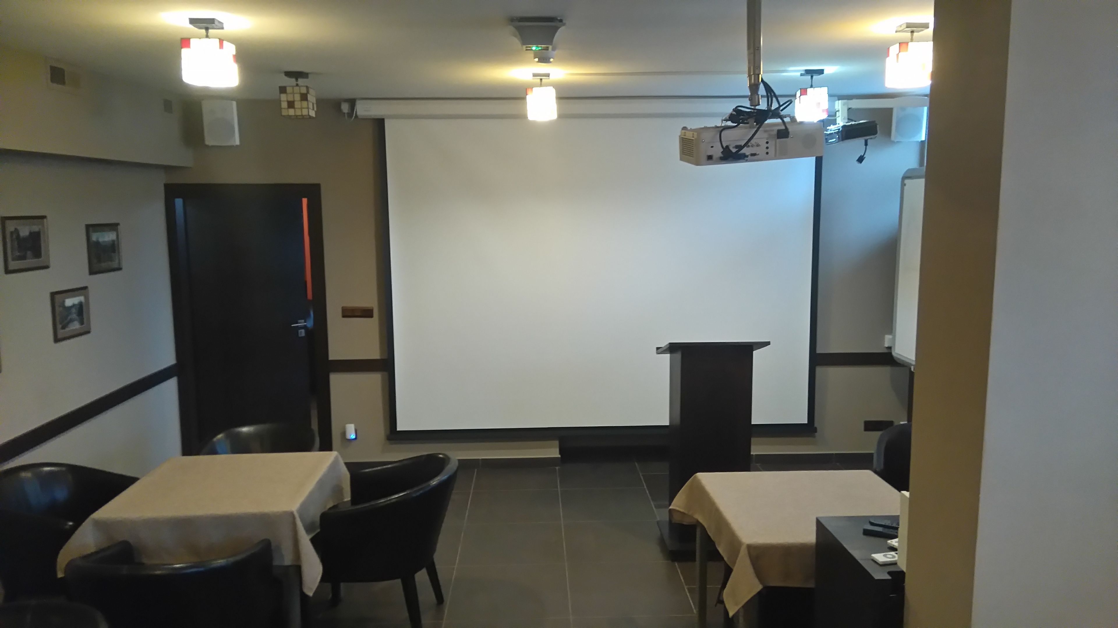 Ein Konferenzraum mit Projektionsleinwand, einem Rednerpult und Tischen mit Stühlen.