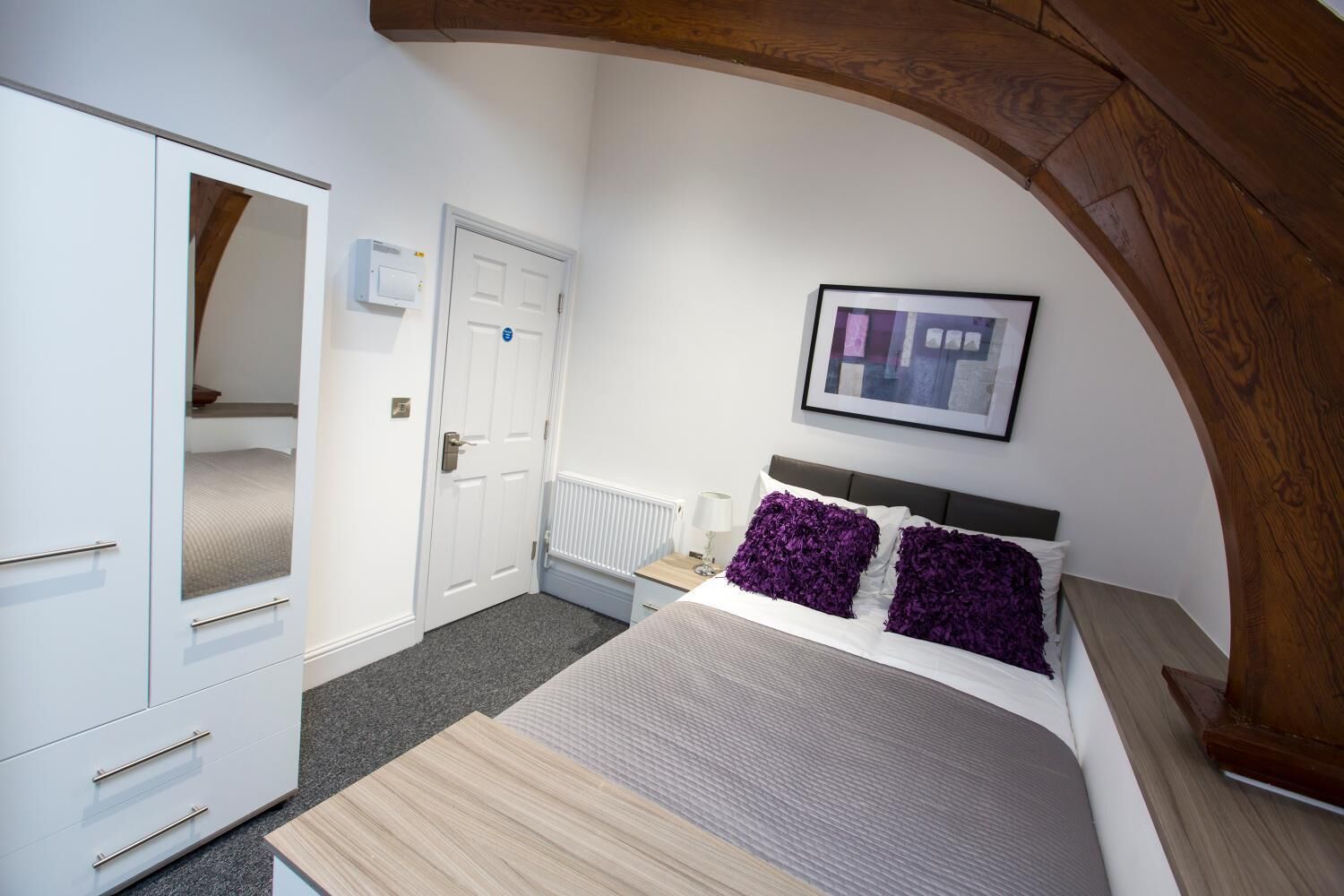 A bedroom with a bed, a wardrobe, a door, a radiator, and a framed picture on the wall.