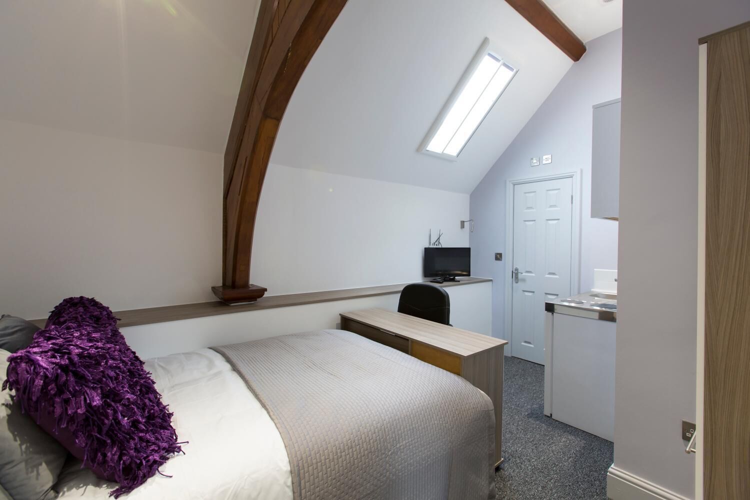 Een hotelkamer met een bed, een bureau, een stoel, een televisie en een kitchenette.