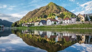 A lakeside town with buildings reflecting on the water, surrounded by a forested hill. - Villa Home & Garden Lasko (Lasko)