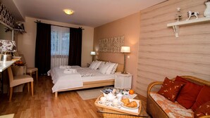 A cozy hotel room with a bed, a dining area, a wicker sofa, and a breakfast tray with croissants. - Villa Home & Garden Lasko (Lasko)
