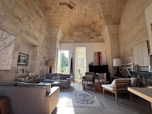 A spacious living room with stone walls, a fireplace, and a view through an open door. - Lu Leccio (Lecce)