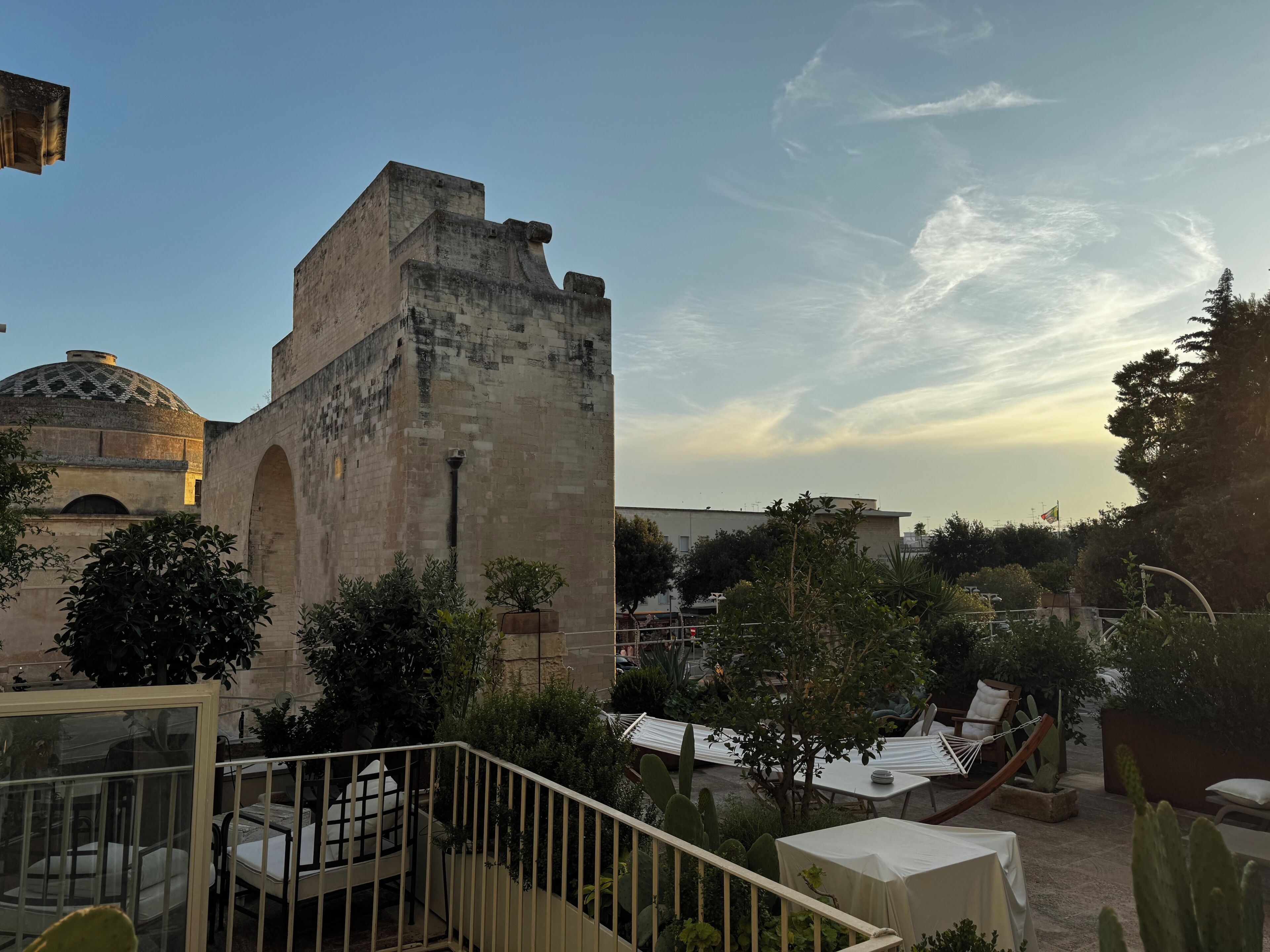 Un patio con una torre de piedra, mobiliario exterior y una estructura abovedada.