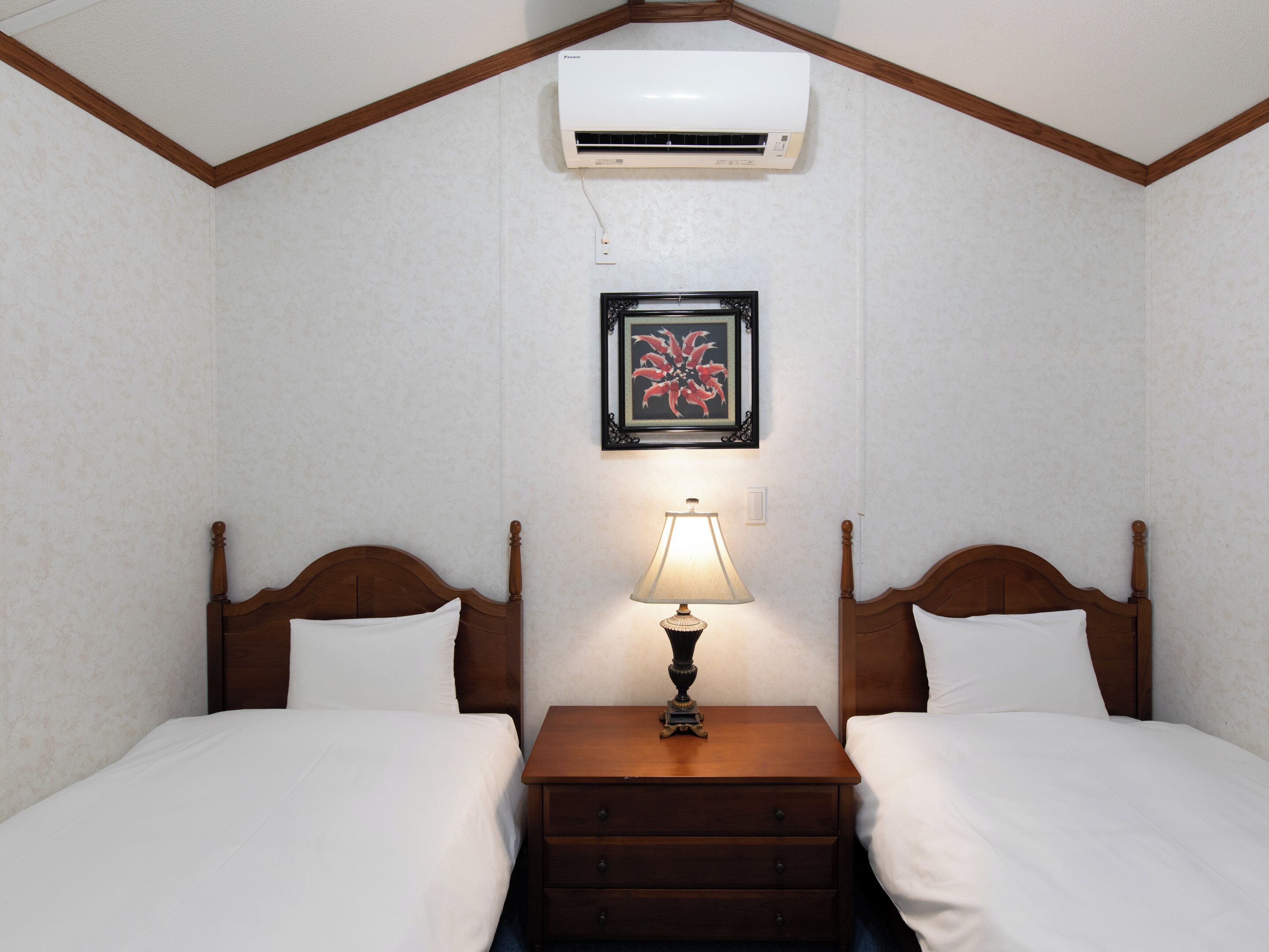 Une chambre d’hôtel avec deux lits, une table de chevet avec une lampe, un climatiseur et un tableau encadré au mur.