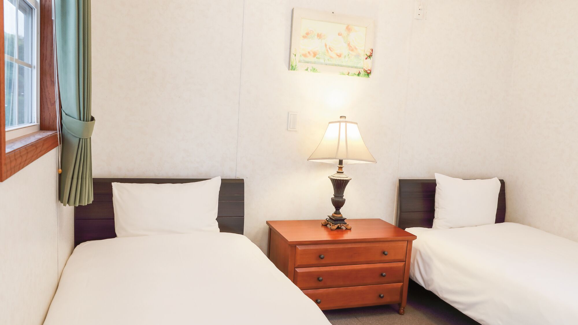 Ein Hotelzimmer mit zwei Betten, einem Nachttisch mit Lampe, einem Fenster mit Vorhängen und einem Gemälde an der Wand.