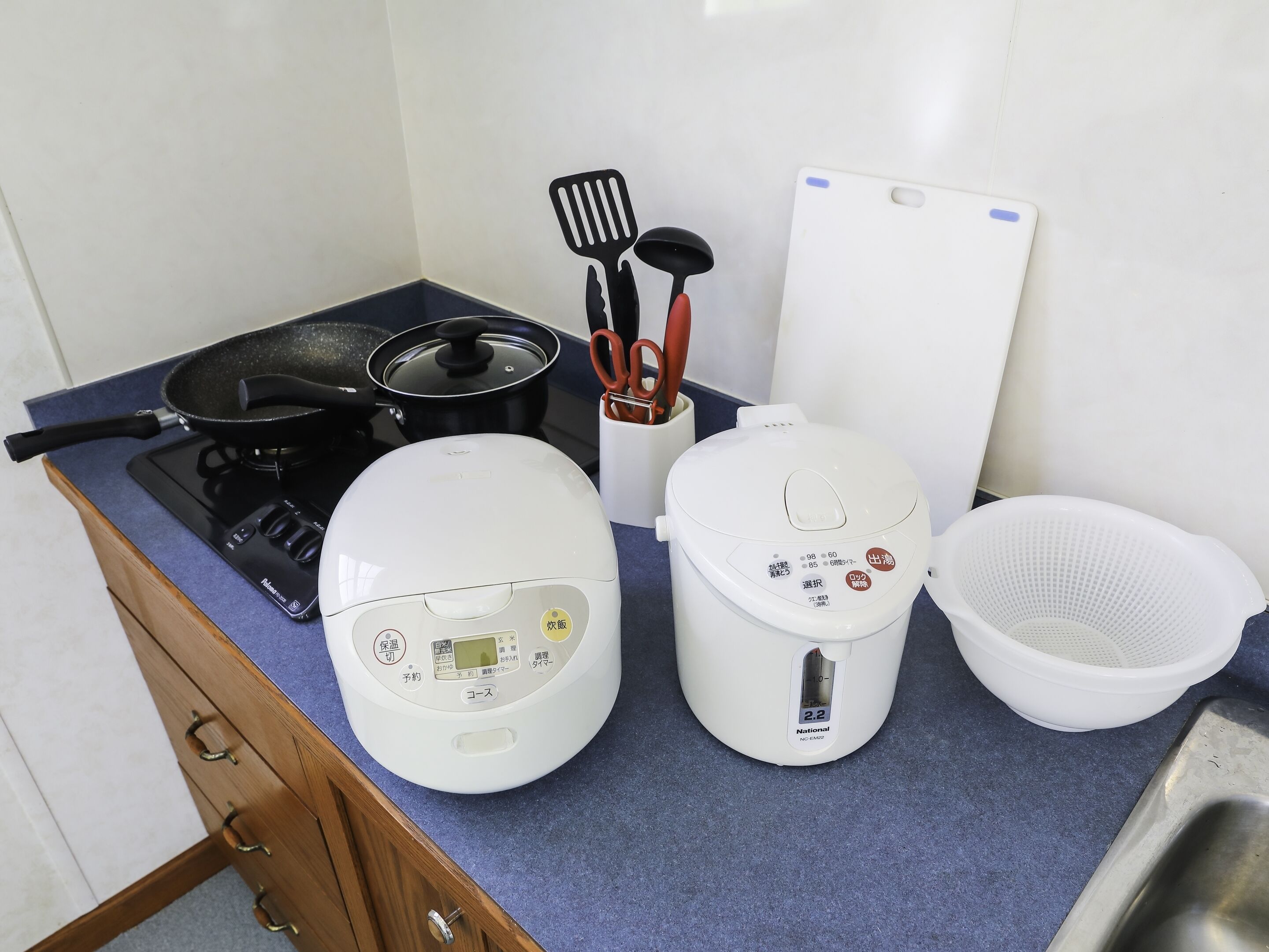 A kitchen with a stove, a rice cooker, a pot, and a colander.