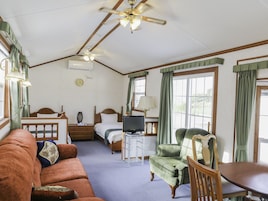 A room with a bed, a TV, a green armchair, a wooden table, and a ceiling fan.