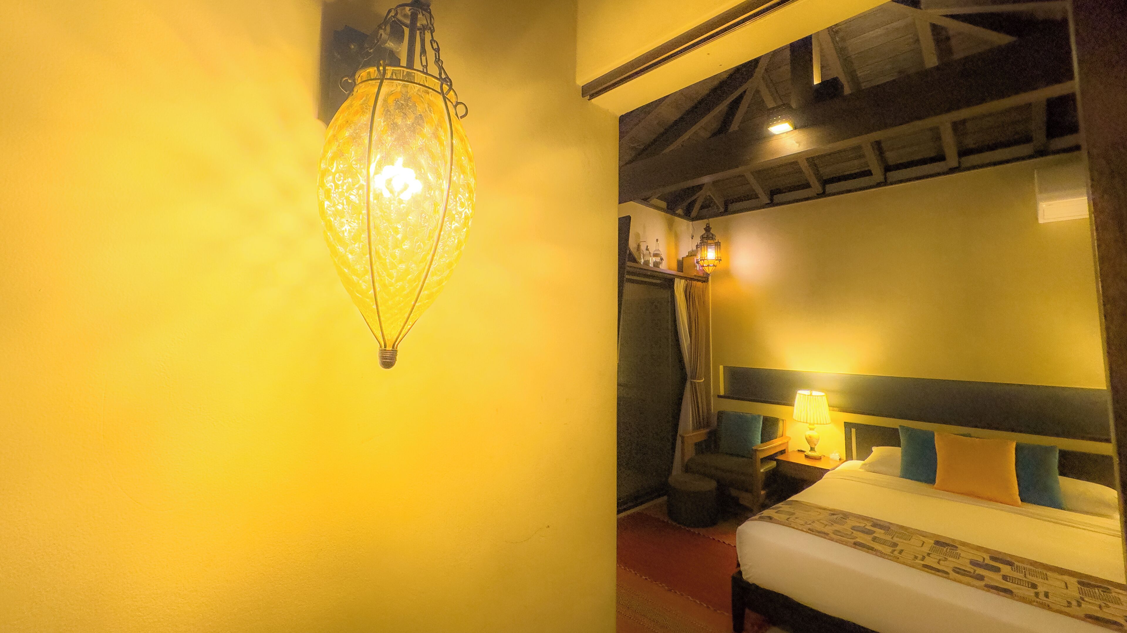 Une pièce comprenant un lit, un luminaire fixé au mur et un plafond avec des poutres apparentes.
