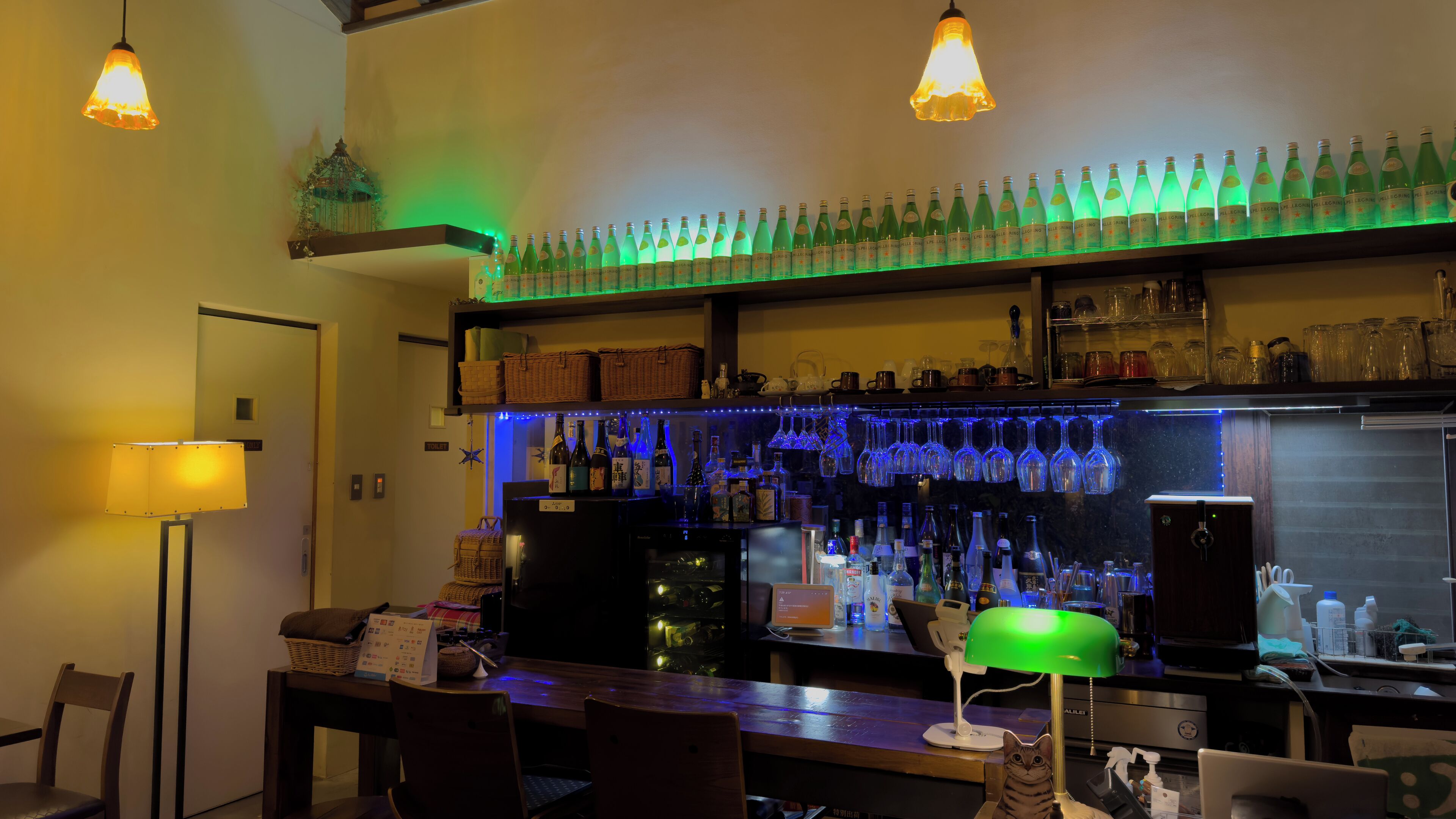 A bar area with shelves of bottles, a computer, and a cat figurine.