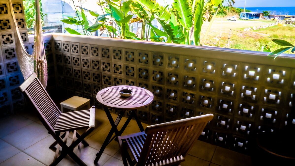 A balcony with a patterned wall, a hammock, a small round table with a bowl, and two chairs.