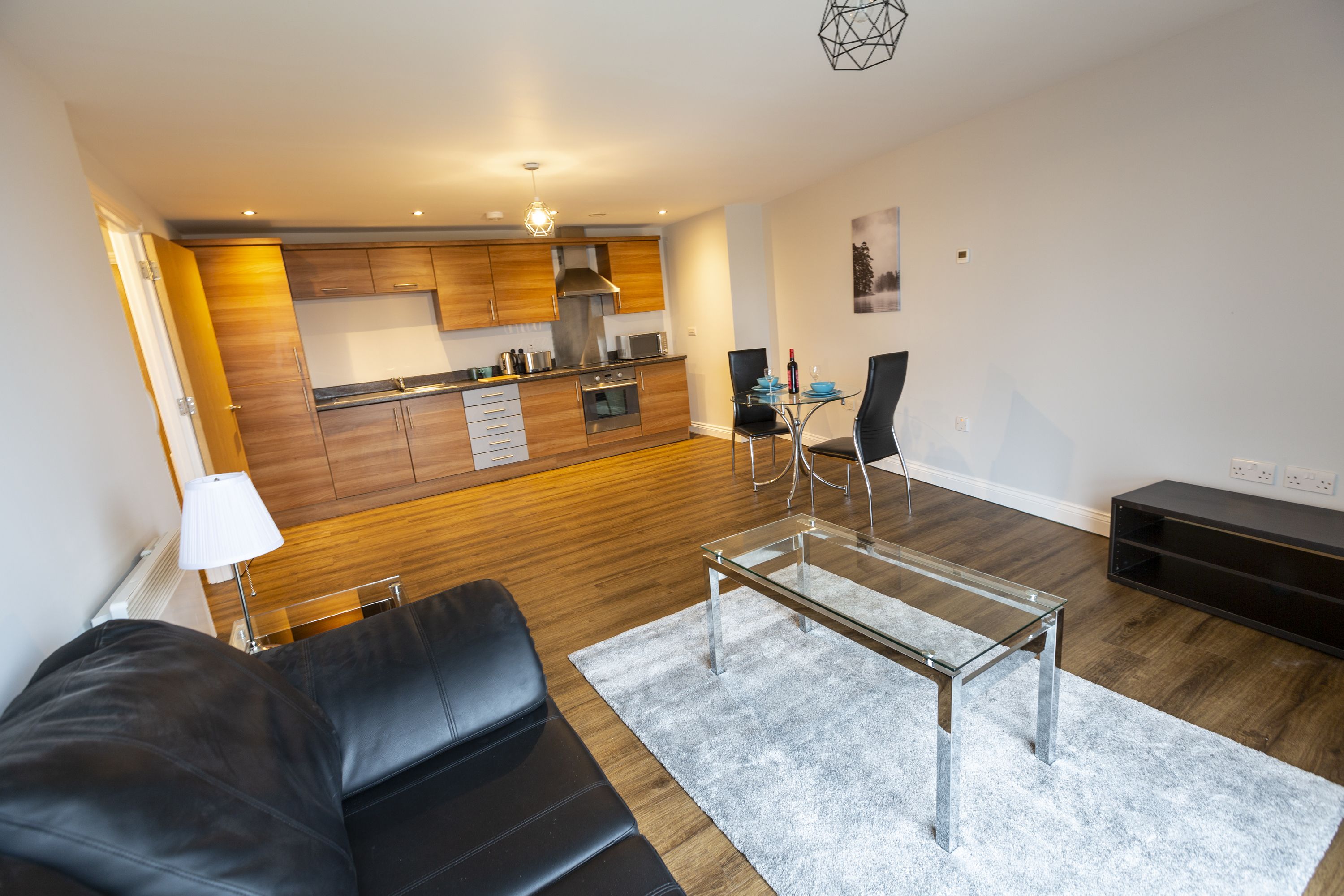 A modern living room with a glass coffee table, a black leather sofa, and a dining area with a table and chairs.