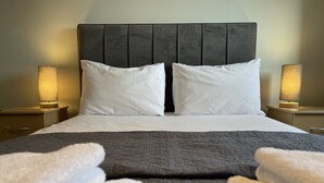 Un lit bien fait, avec une couverture grise, des oreillers blancs et deux lampes de chevet.