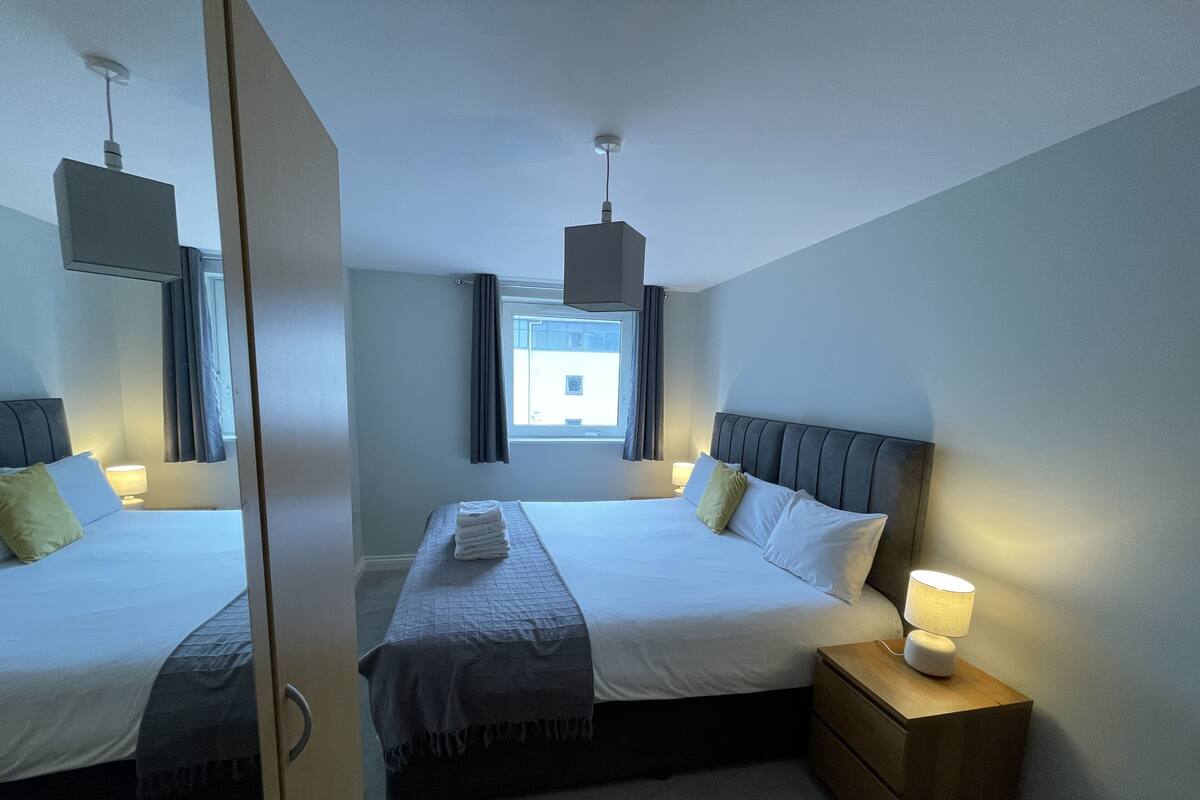 Une chambre d’hôtel avec deux lits, une table de chevet, une lampe et une fenêtre avec des rideaux.