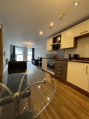 A modern kitchen with a glass dining table, built-in oven, and stainless steel appliances.