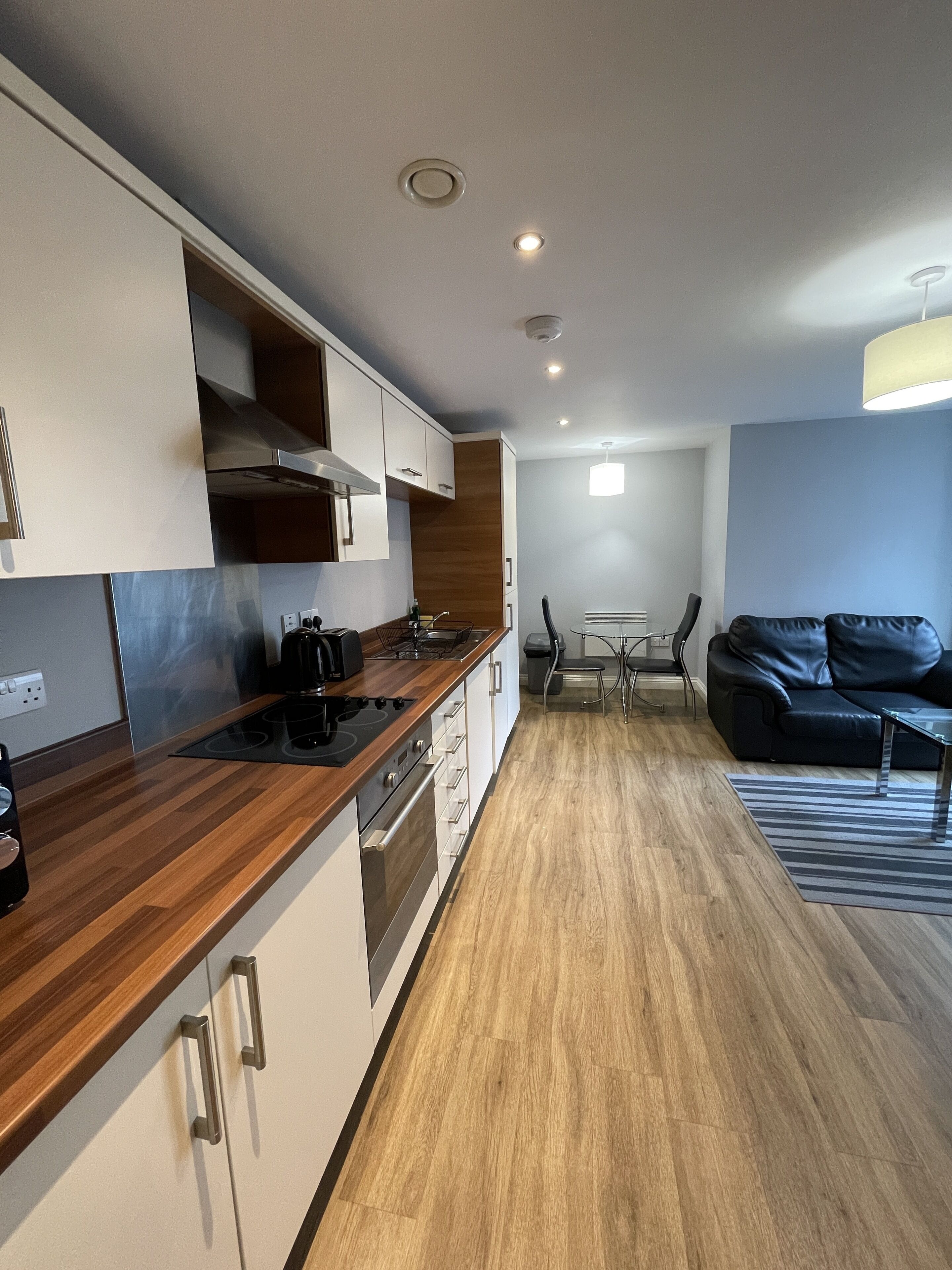 Una cucina moderna con piani in legno, pensili integrati e una zona pranzo con un divano in pelle nera e un tavolo in vetro.