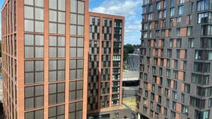 Un bâtiment moderne à plusieurs étages, doté d’une façade à motifs géométriques de fenêtres et d’une cour intérieure aménagée avec des espaces pour s’asseoir et de la verdure.