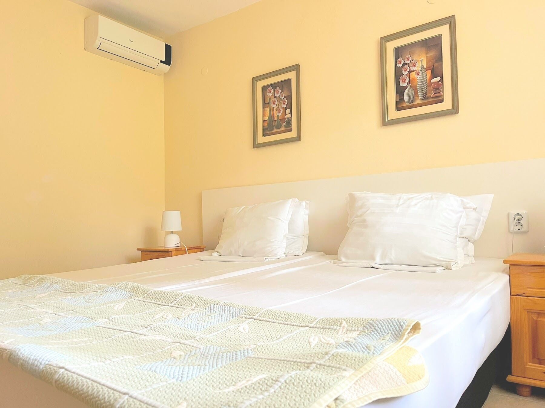 A hotel room with a bed, two bedside tables, a lamp, and two framed pictures on the wall.