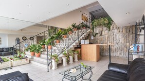 Un hall d’entrée spacieux avec un escalier, de nombreuses plantes en pot, un comptoir de réception et des sièges en cuir.