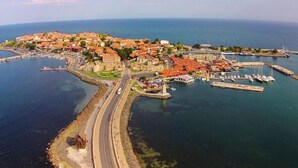 Vue aérienne d’une ville côtière avec un port de plaisance, une route menant à la ville et des bâtiments aux toits rouges.
