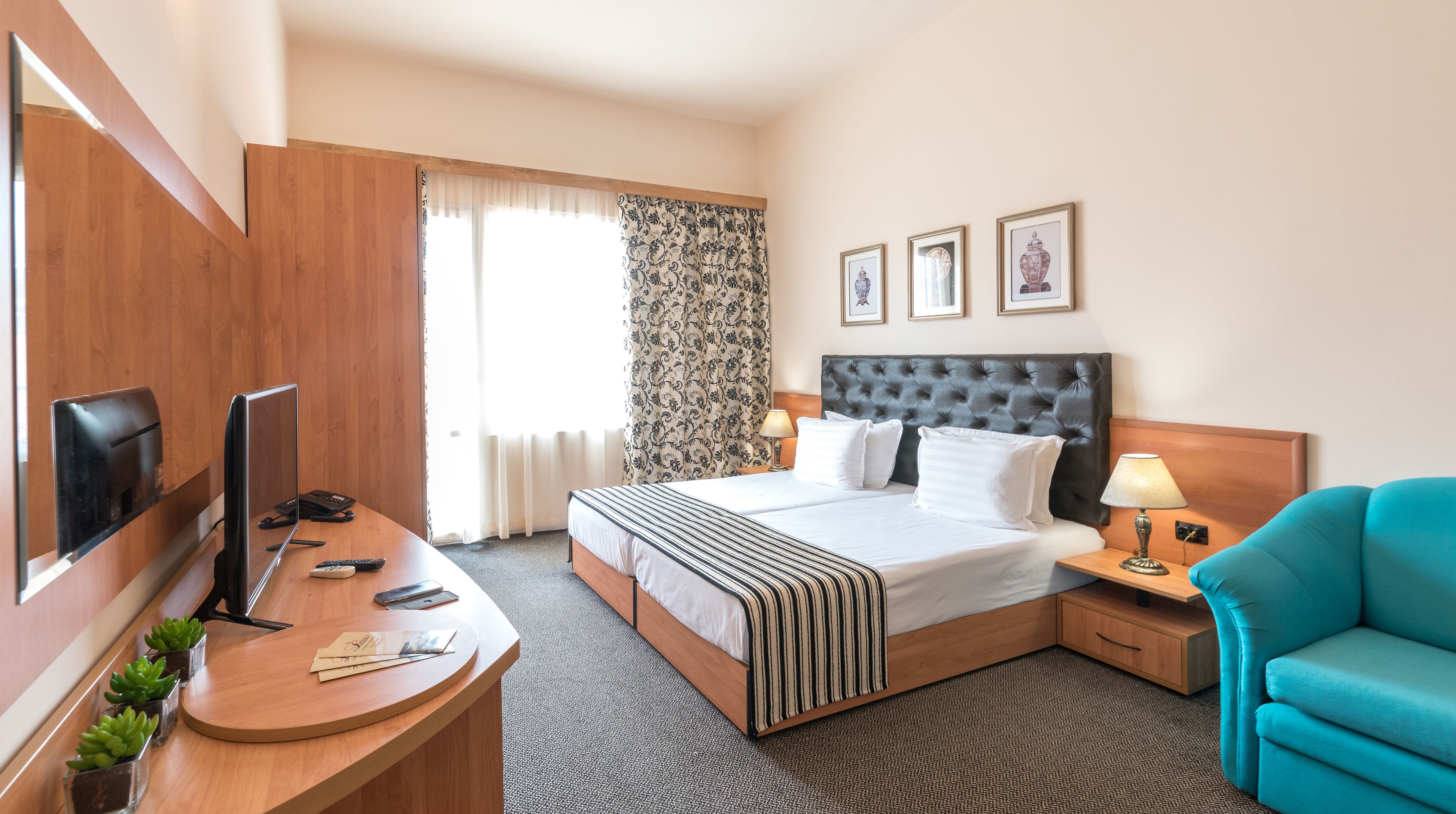 Habitación de hotel con cama, escritorio con televisor, silla y ventana con cortinas.