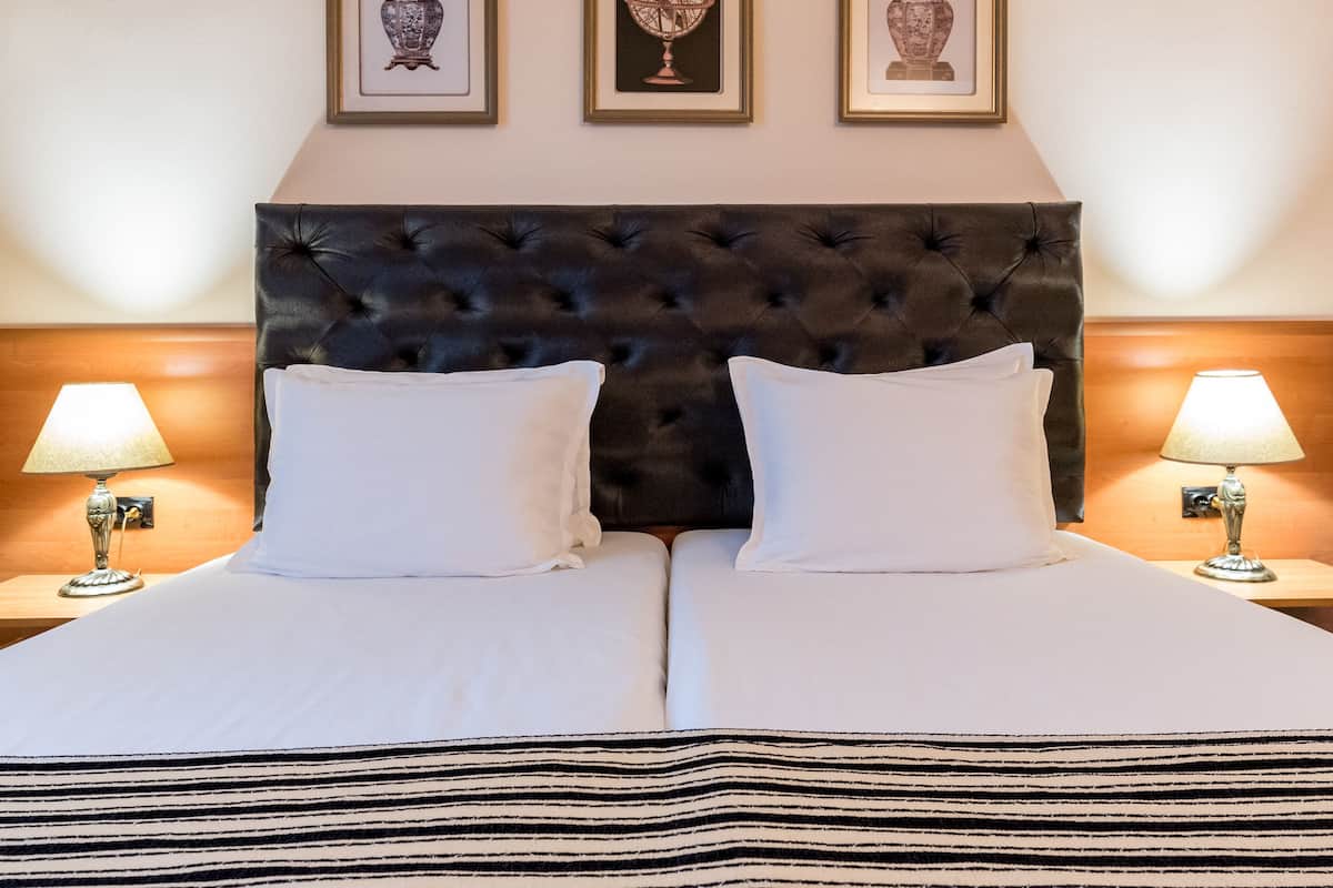Una cama doble con cabecera capitonada, dos mesitas de noche con lámparas y tres cuadros enmarcados en la pared de arriba.