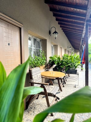 A covered outdoor seating area with a table and chairs, potted plants, and a building with a tiled entrance. - Hotel Lotus (Sunny Beach)