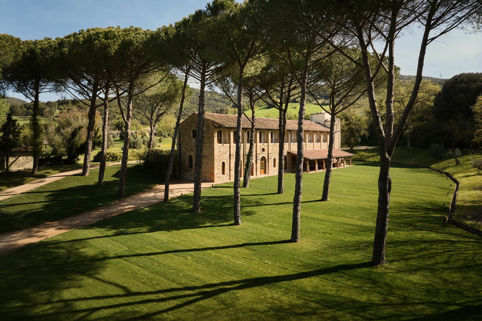 Un edificio in pietra con tetto in tegole, immerso in un prato curato e circondato da alberi alti.
