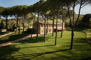 A stone building with a tiled roof, surrounded by a well-maintained lawn and tall trees. - UNA Hotels Monterufoli Wine Country (Monteverdi Marittimo)