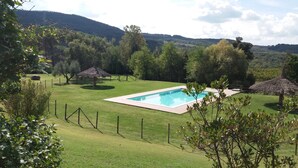 A rectangular swimming pool surrounded by a fenced grassy area with trees and hills in the background. - UNA Hotels Monterufoli Wine Country (Monteverdi Marittimo)