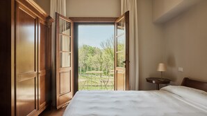 A bedroom with a large bed, an open door leading to a balcony, and a small table with a lamp. - UNA Hotels Monterufoli Wine Country (Monteverdi Marittimo)