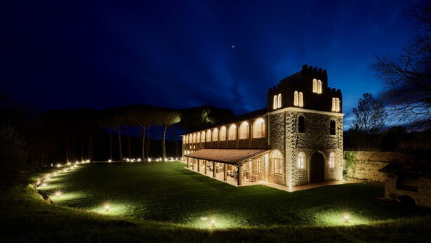 A stone building with a tower, illuminated by lights, surrounded by a well-lit lawn. - UNA Hotels Monterufoli Wine Country (Monteverdi Marittimo)