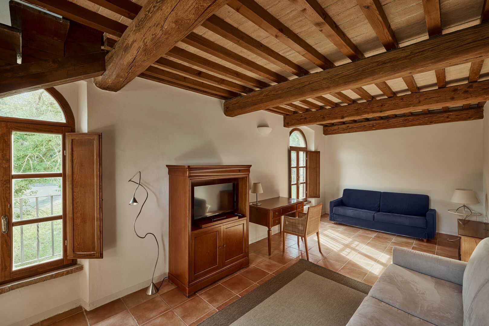 A living room with a wooden ceiling, a TV, a blue sofa, and a dining area with a table and chairs.