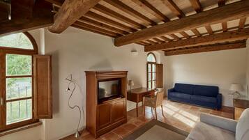 A living room with a wooden ceiling, a TV, a blue sofa, and a dining area with a table and chairs.