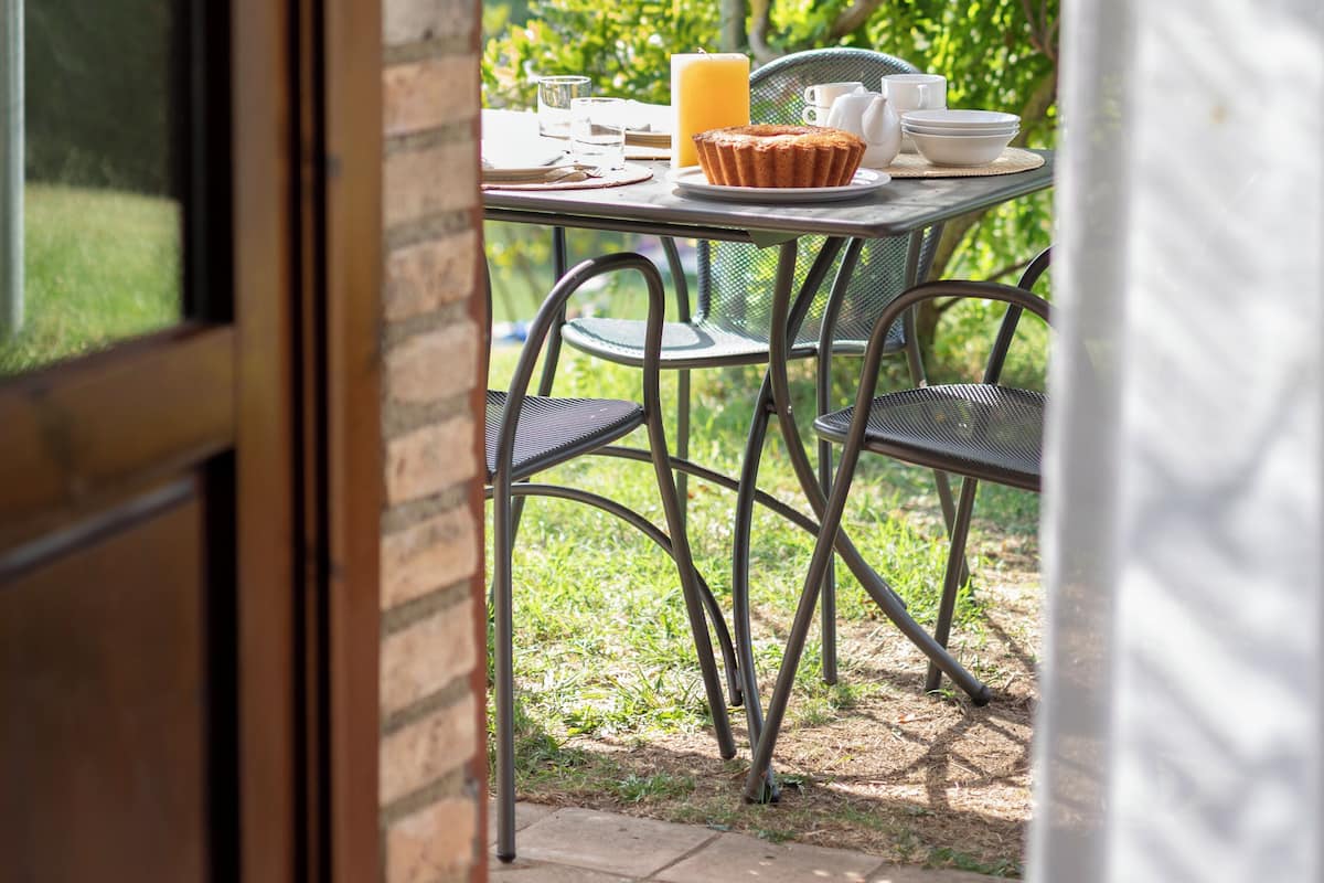 Un patio exterior con una mesa dispuesta para el desayuno, que incluye un muffin, tazas de café y un vaso de jugo.