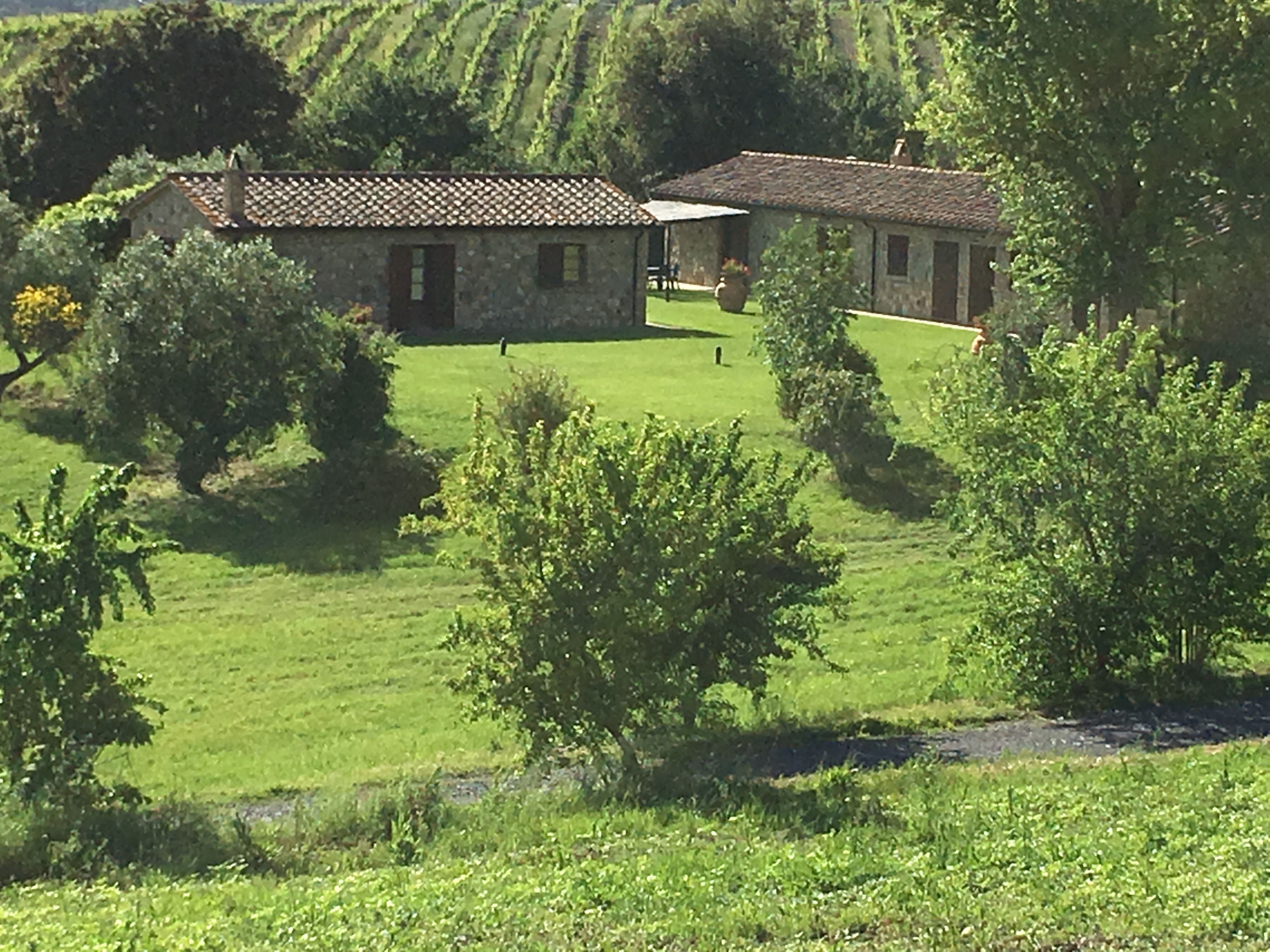 A stone building with a tiled roof, surrounded by lush green fields and trees.