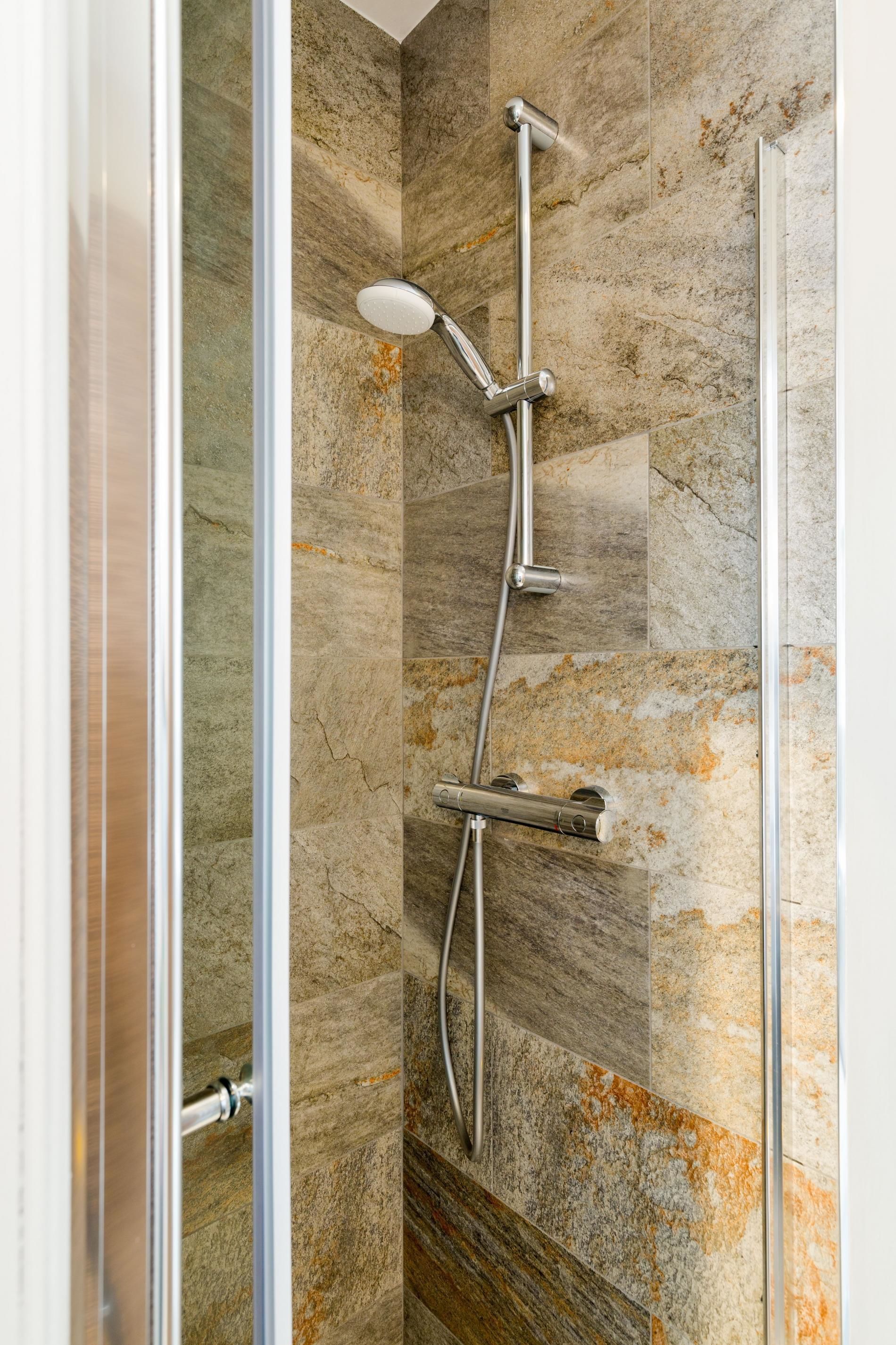 A shower with a handheld showerhead and a wall-mounted control panel.