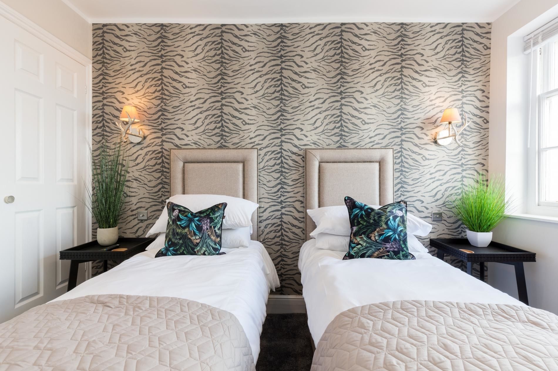 A hotel room with two beds, zebra-striped wallpaper, bedside lamps, and potted plants.