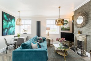 A modern living room with a teal sofa, a fireplace, and a large abstract painting. - L-Spa Boutique Apartment No. 5 (Royal Leamington Spa)