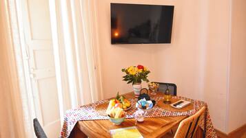 Uma mesa de jantar com toalha estampada, um vaso com flores e diversos alimentos.