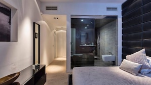 Ein modernes Schlafzimmer mit Bett, Nachttisch, Spiegel und Blick ins Badezimmer.