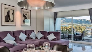 Ein modernes Wohnzimmer mit einem violetten Sofa, einem Esstisch für vier Personen und einem Balkon mit Blick auf die Berge.