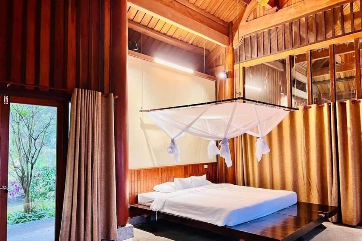 A wooden cabin-style room with a bed, a window with curtains, and a view of trees.