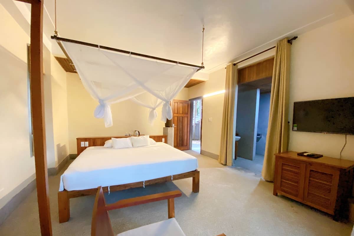 A bedroom with a bed, a wooden chair, a television, and a bathroom visible through an open door.