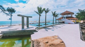 A resort pool area with a clear view of the ocean, palm trees, and a gazebo structure. - Quynh Vien Resort (Thach Khe)