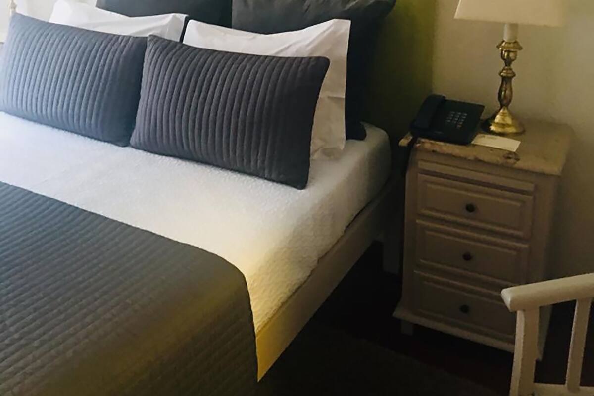 Een hotelkamer met een groen bekleden hoofdeinde, een bed met witte en donkergrijze lakens, twee nachtkastjes met lampen, en een kleine witte stoel.