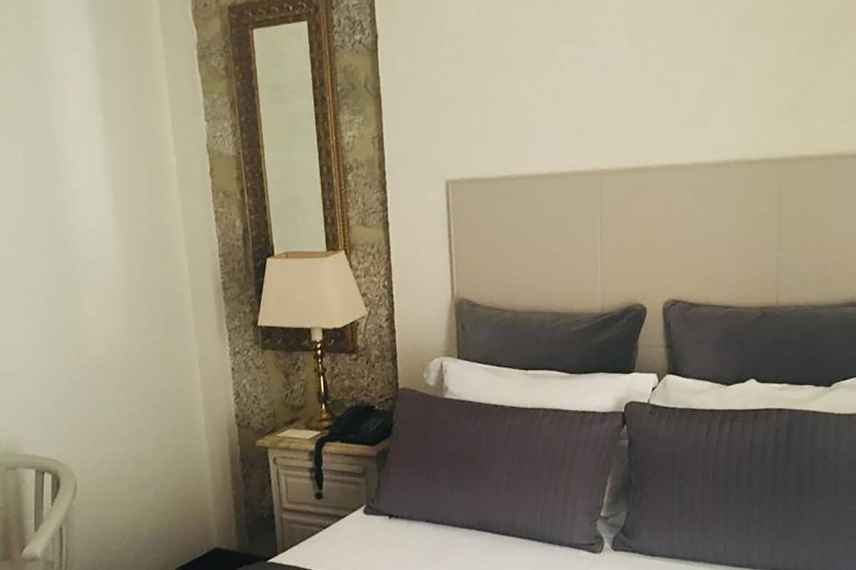 Een hotelkamer met een bed, nachtkastje met lamp, een stoel en een spiegel.