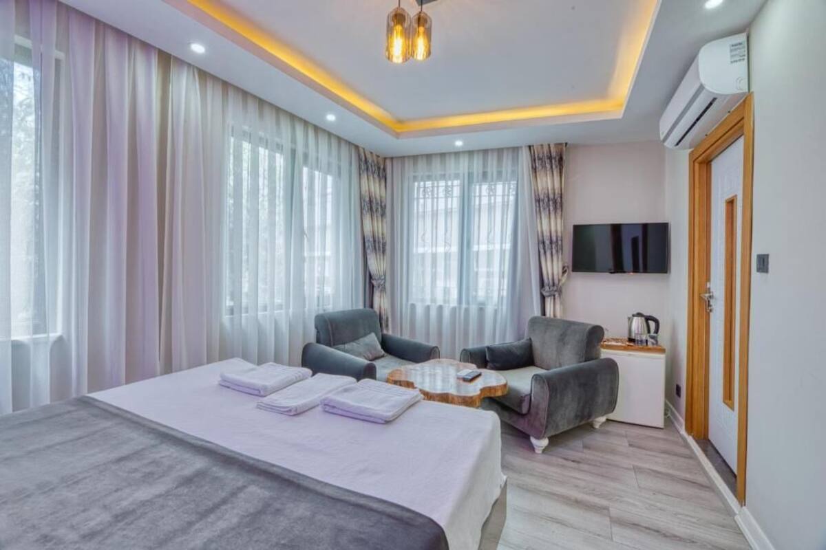 A modern hotel room with a large bed, two armchairs, a small coffee table, and a TV.