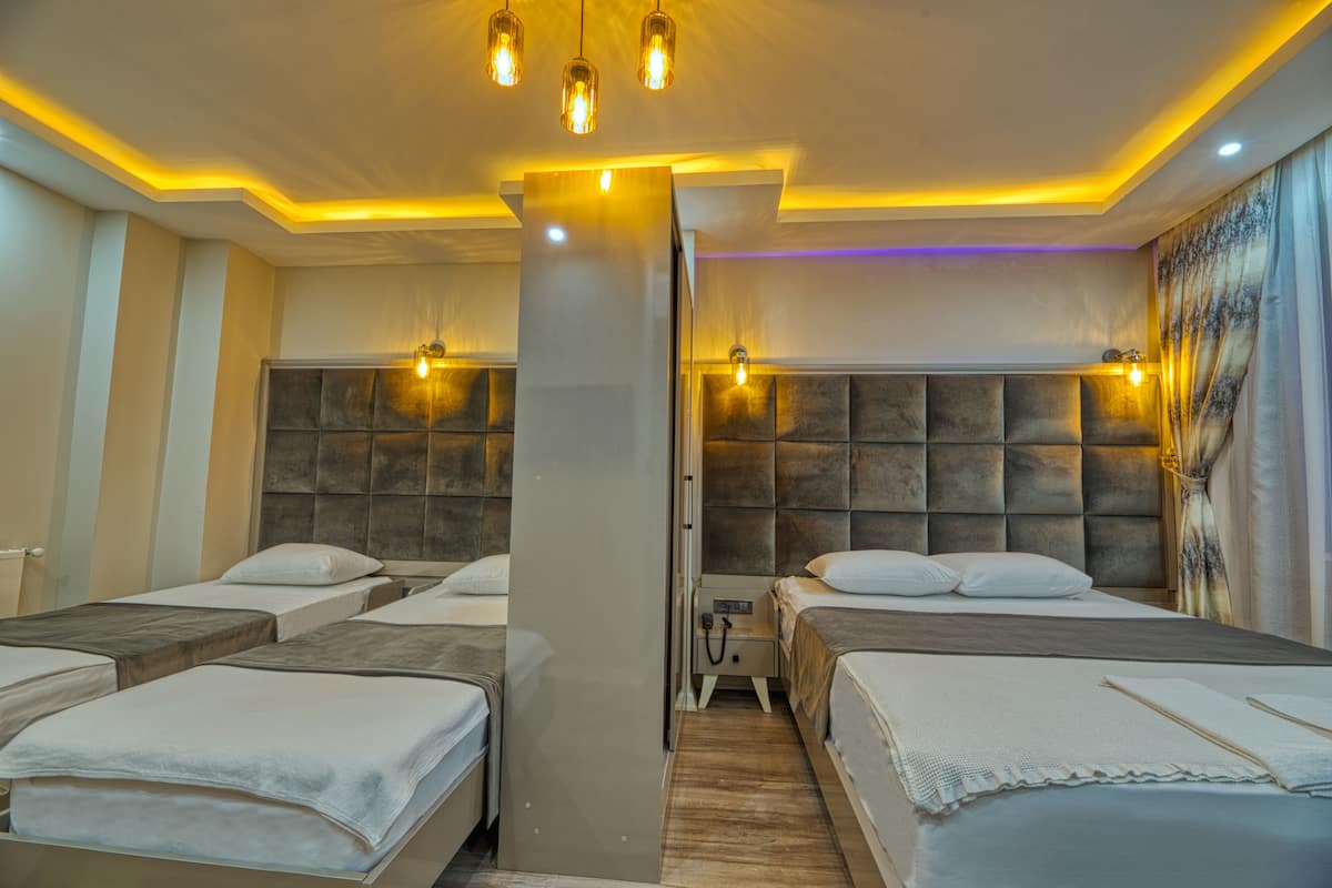 A hotel room with four beds arranged in a U-shape, a central pillar, and a headboard with built-in lighting.